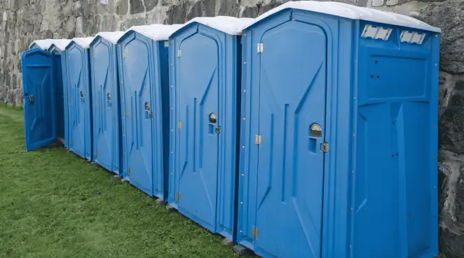 Row of blue portable toilets lined up on grass against a stone wall for event sanitation in Lincoln, NE
