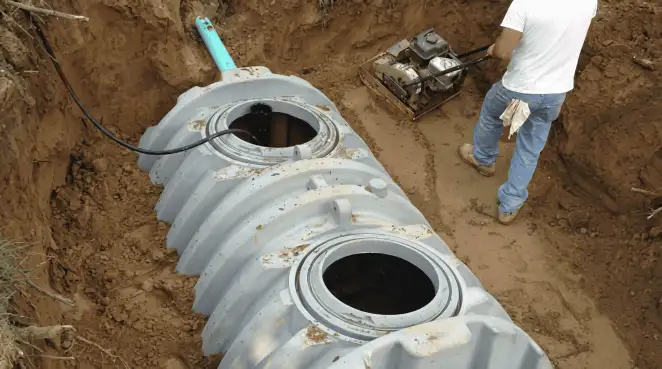 Septic tank installation showing a technician compacting soil around a new poly septic tank in an excavation pit in Lincoln, NE